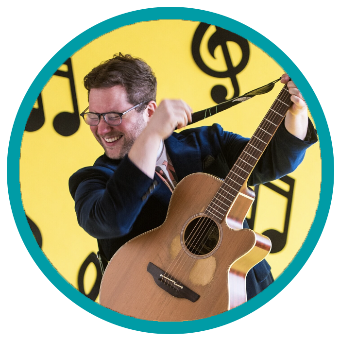 Jesse Jukebox performing guitar infront of a yellow background.